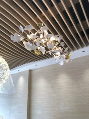 Elegant gold and white gingko leaf chandelier pendant lamp hanging from a modern wooden slat ceiling
