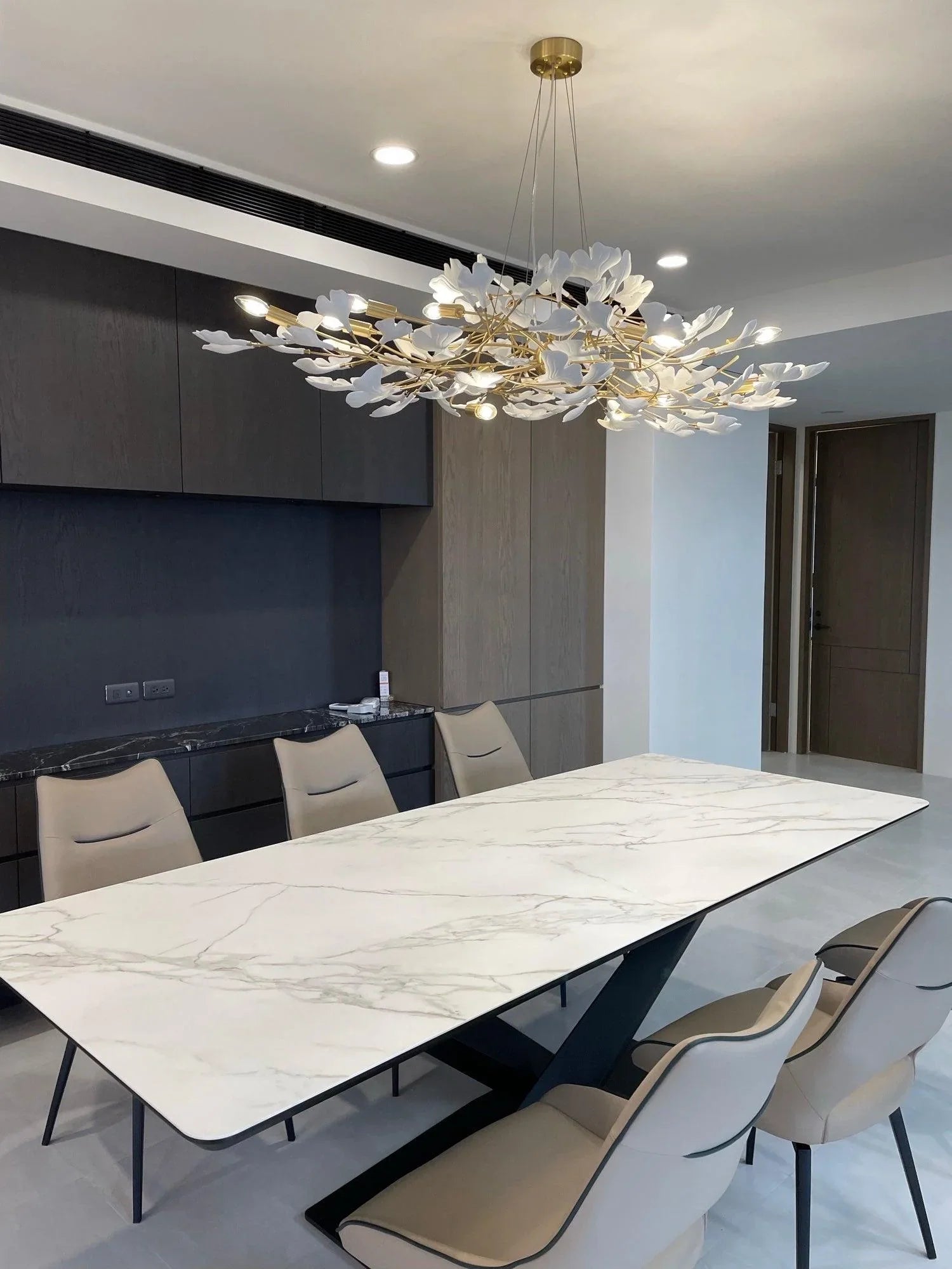 Modern dining room with a large white marble table, beige chairs, and a gold white Gingko chandelier pendant lamp