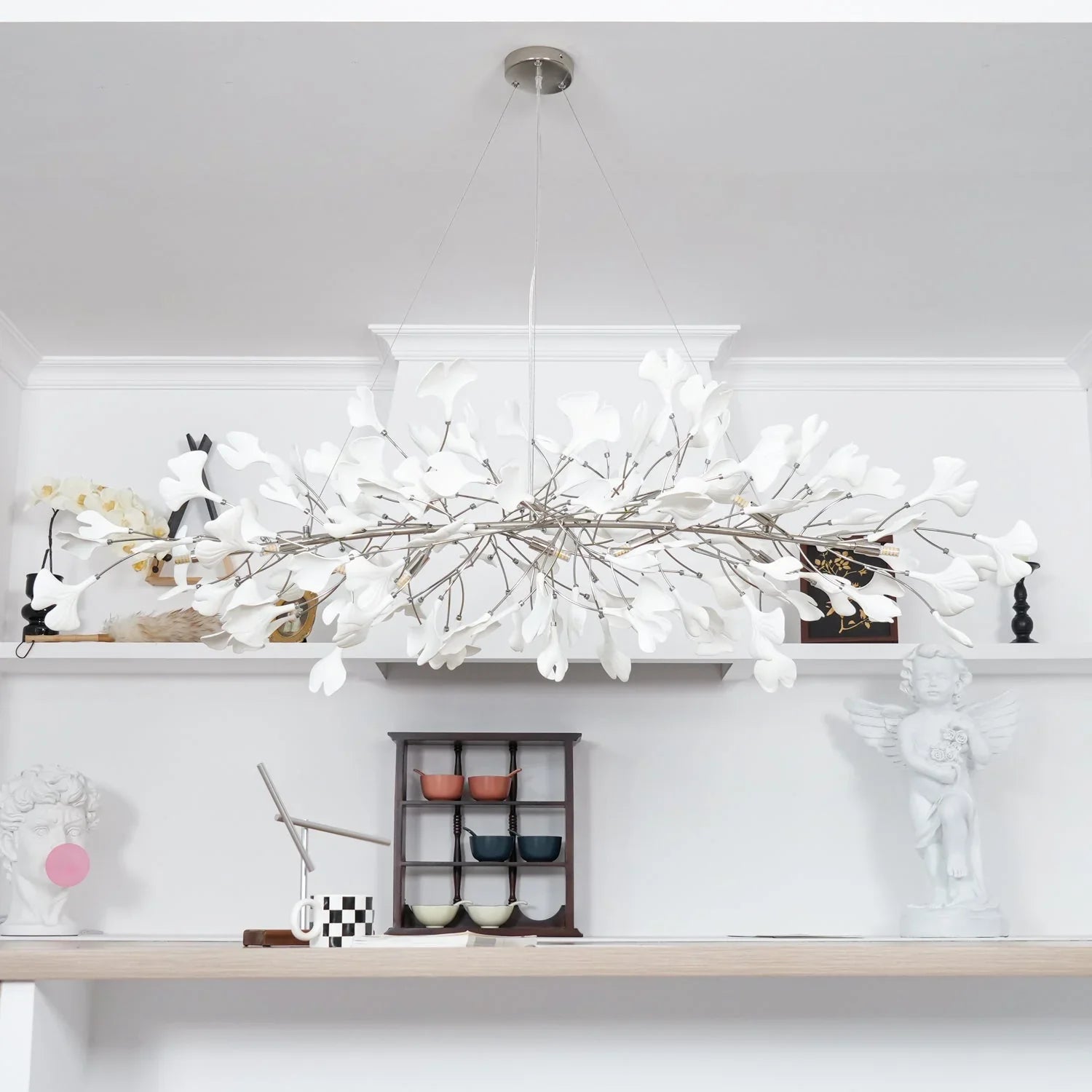 Modern gold and white ginkgo chandelier with delicate leaf design hanging above minimalist shelf decor