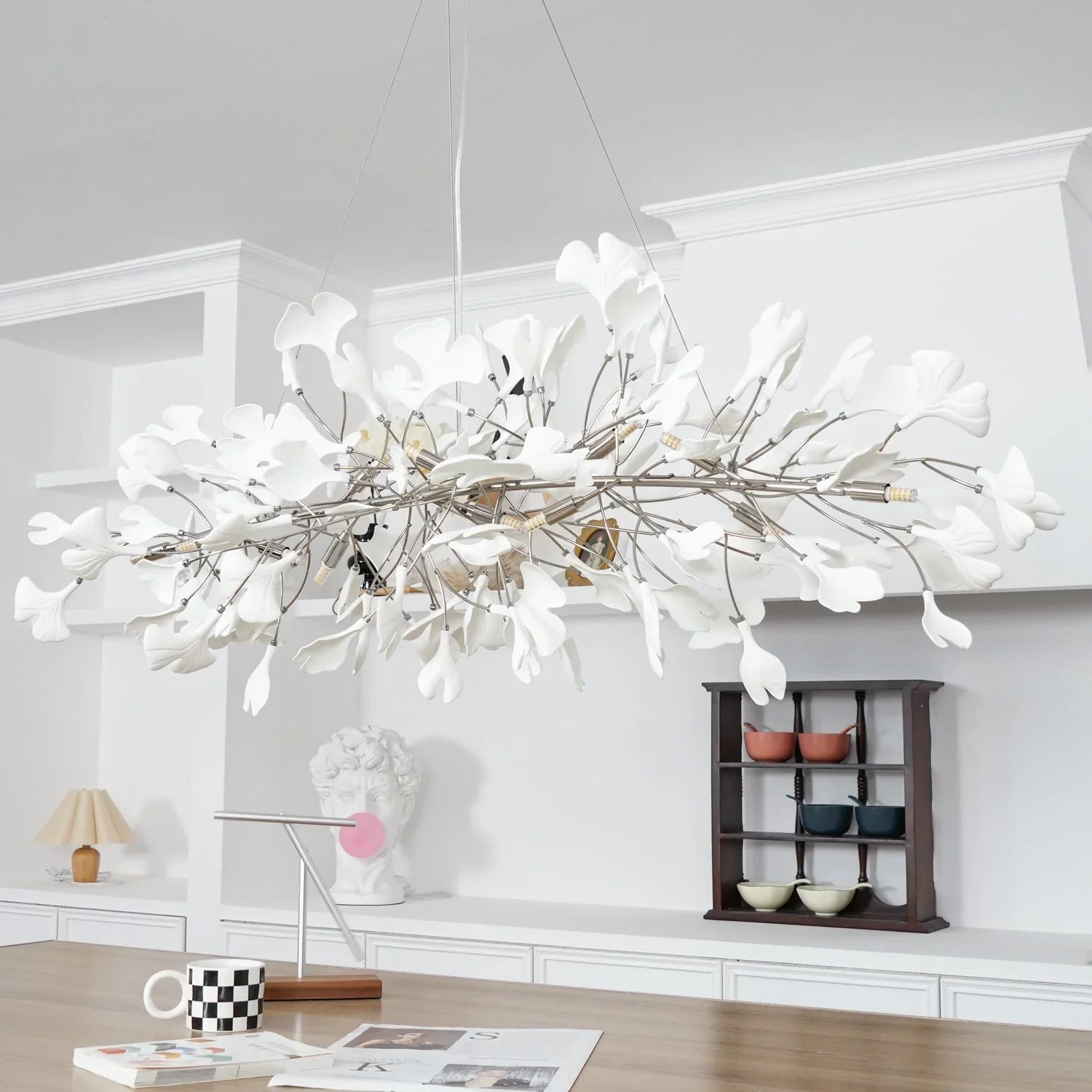 Modern white ginkgo leaf chandelier pendant lamp hanging in a bright minimalist room with wooden table and decorative art pieces