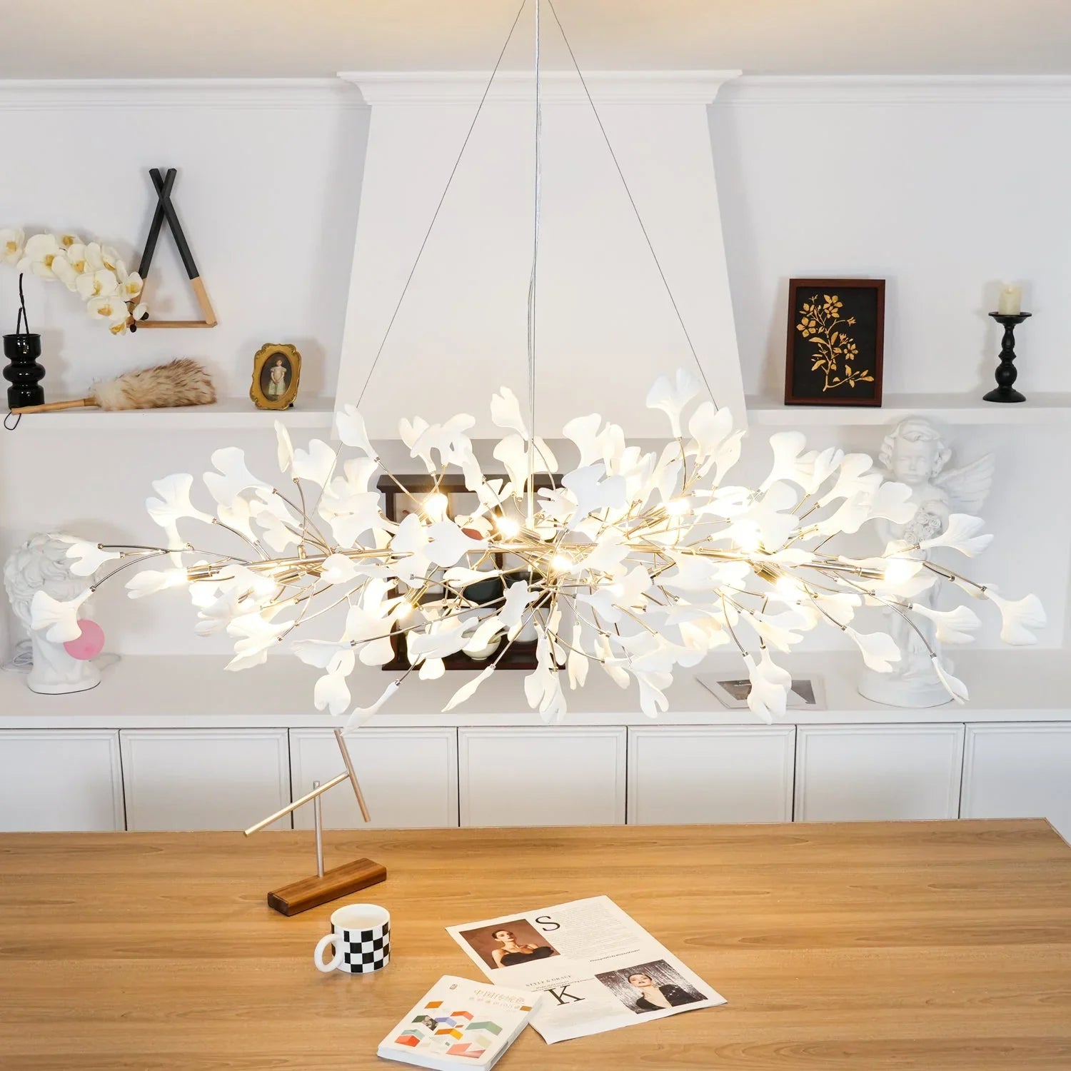 Modern gold and white ginkgo leaf chandelier pendant lamp hanging above wooden table in stylish room