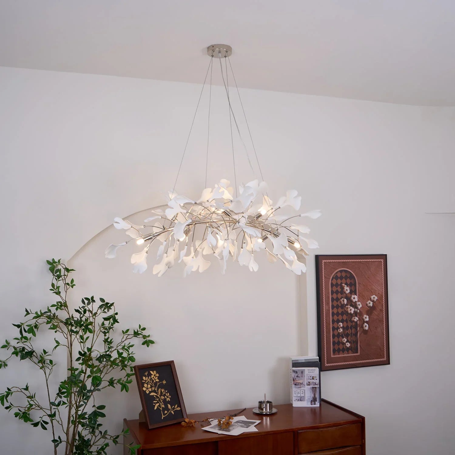 Modern gold and white gingko pendant chandelier hanging above wooden sideboard with plant and framed art