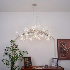 Modern gold and white ginkgo leaf chandelier pendant lamp above wooden table with green plant and framed art