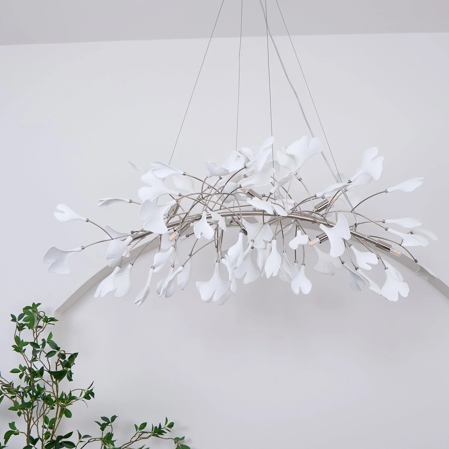 Modern gold and white pendant chandelier with ginkgo leaf design hanging in minimalist white room