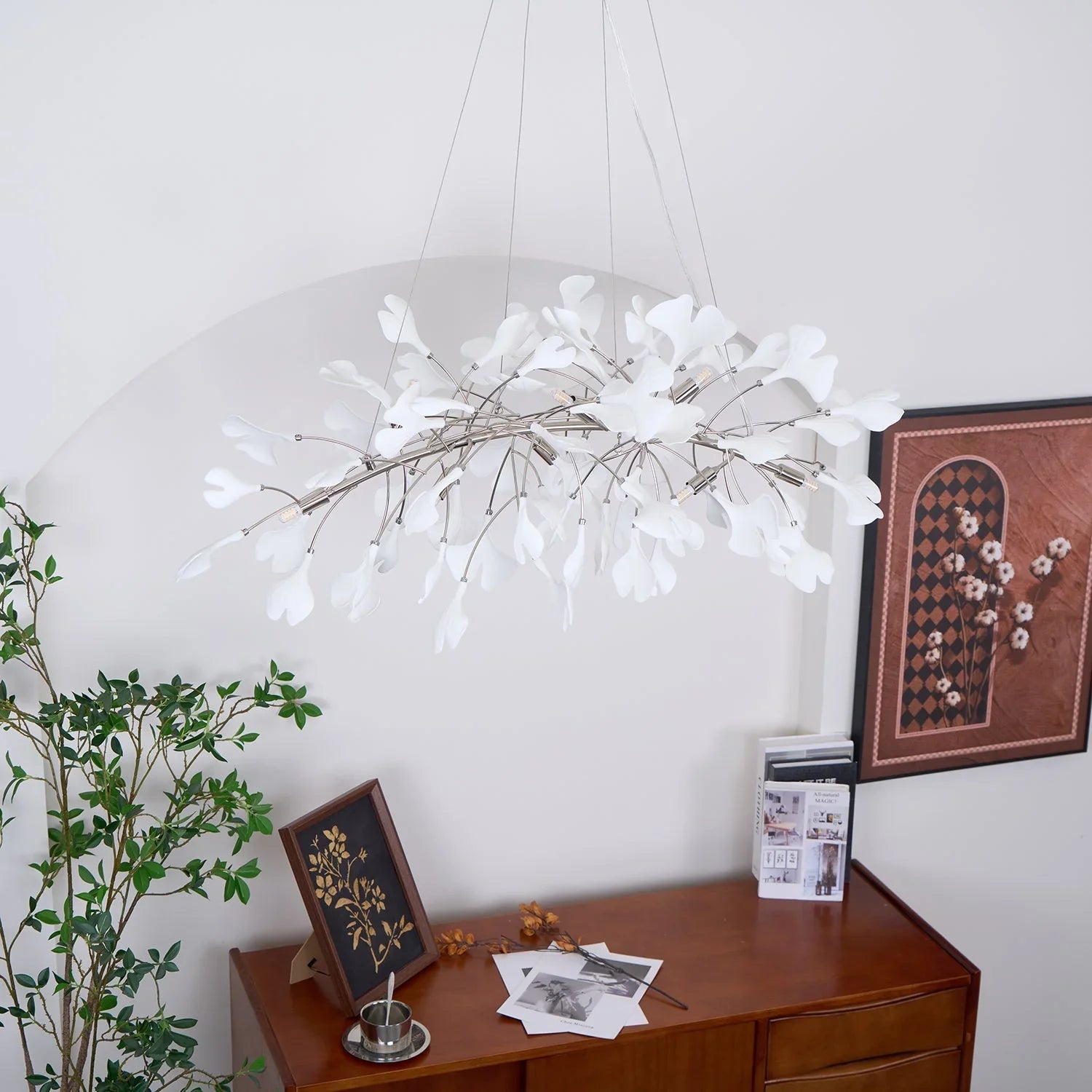 Modern white ginkgo leaf chandelier pendant lamp hanging above wooden sideboard with art and plant