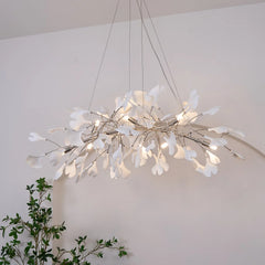 Modern gold and white ginkgo leaf chandelier pendant lamp suspended in a minimal room with plant