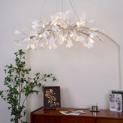Modern white ginkgo leaf chandelier pendant lamp hanging over wooden sideboard with green plant and framed art