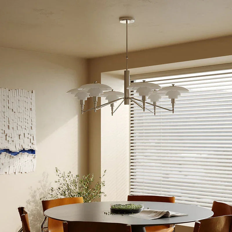 Modern silver pendant chandelier with layered white shades hanging above a round dining table, contemporary interior by YH Lamps.