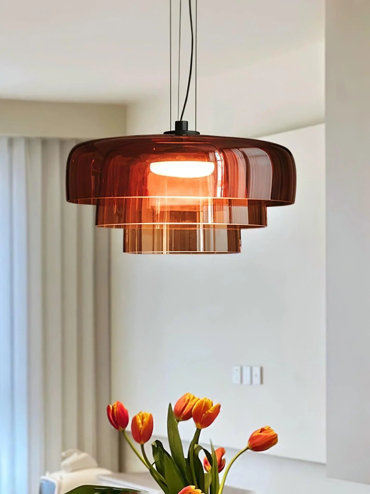 Modern brown glass pendant lamp hanging over table with orange tulips in bright room