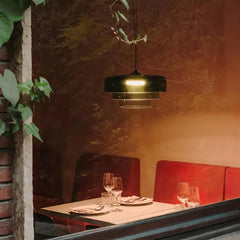 Smoke grey modern pendant lamp with warm light above a restaurant table set with plates, glasses, and red seating