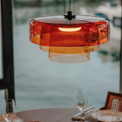 Modern amber glass pendant lamp hanging above a dining table set with glassware and plates near a large window