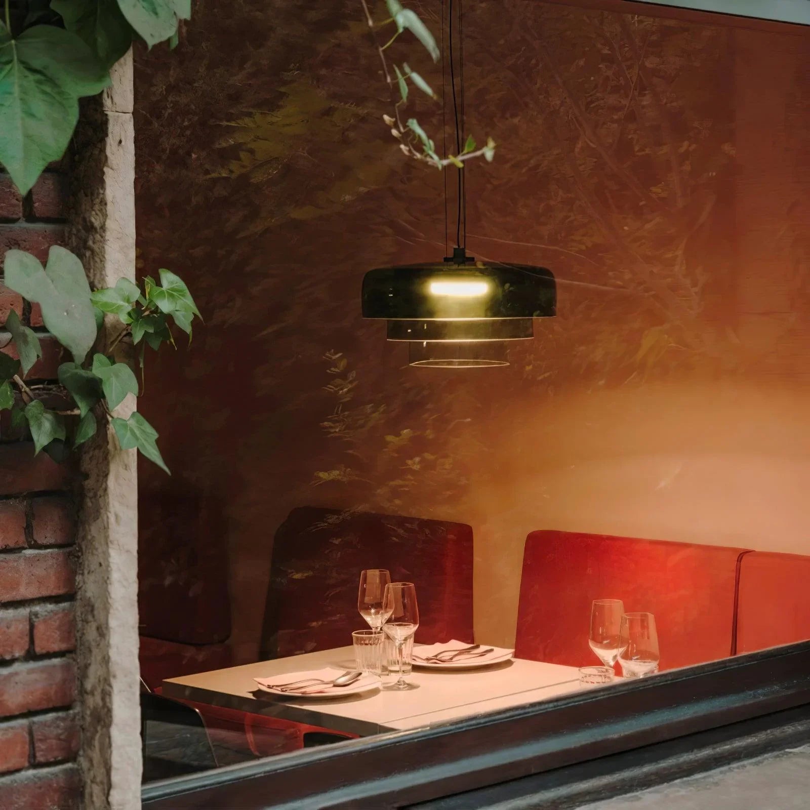 Modern smoke grey pendant lamp with warm light over restaurant table set with plates and glasses
