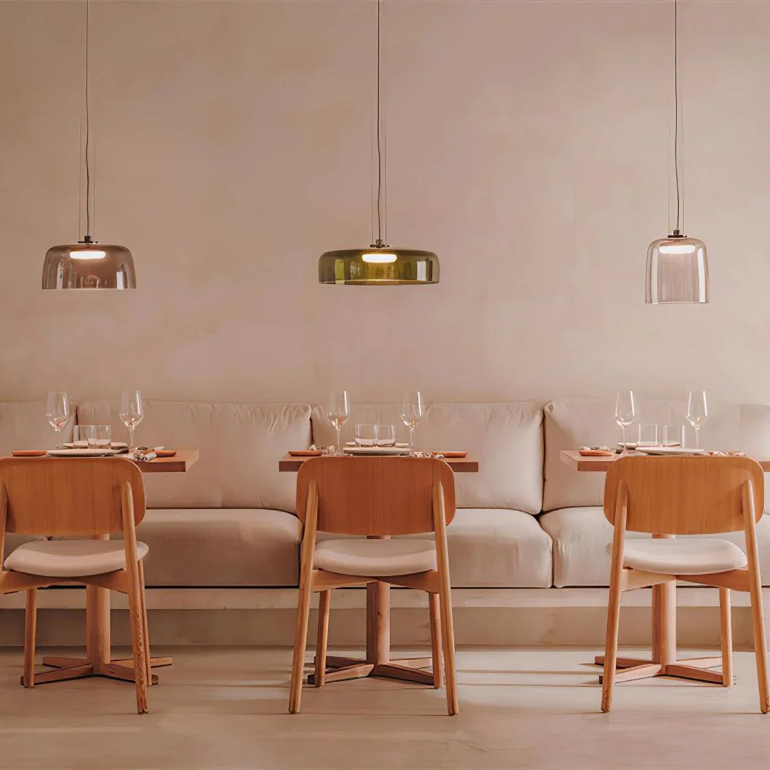 Modern dining area with wooden chairs, soft cushioned bench, and three smoke grey pendant lamps lighting the space