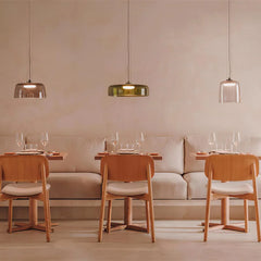 Modern dining area with wooden chairs, soft cushioned bench, and three smoke grey pendant lamps lighting the space