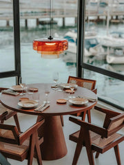 Modern round wooden dining table with four cane chairs and orange pendant lamp over marina view