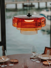 Modern orange glass pendant lamp hanging above a dining table set with wine glasses and plates by a window