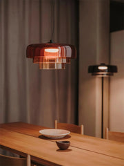 Modern smoke grey pendant lamp with warm light hanging above wooden dining table with ceramic bowl and plate