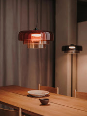 Modern smoke grey pendant lamp hanging over wooden dining table with warm light and ceramic dishes