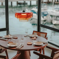 Modern smoke grey pendant lamp with warm light above wooden dining table set with plates and glasses near windows