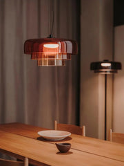 Modern smoke grey glass pendant lamp above wooden dining table with plates in warm ambient light