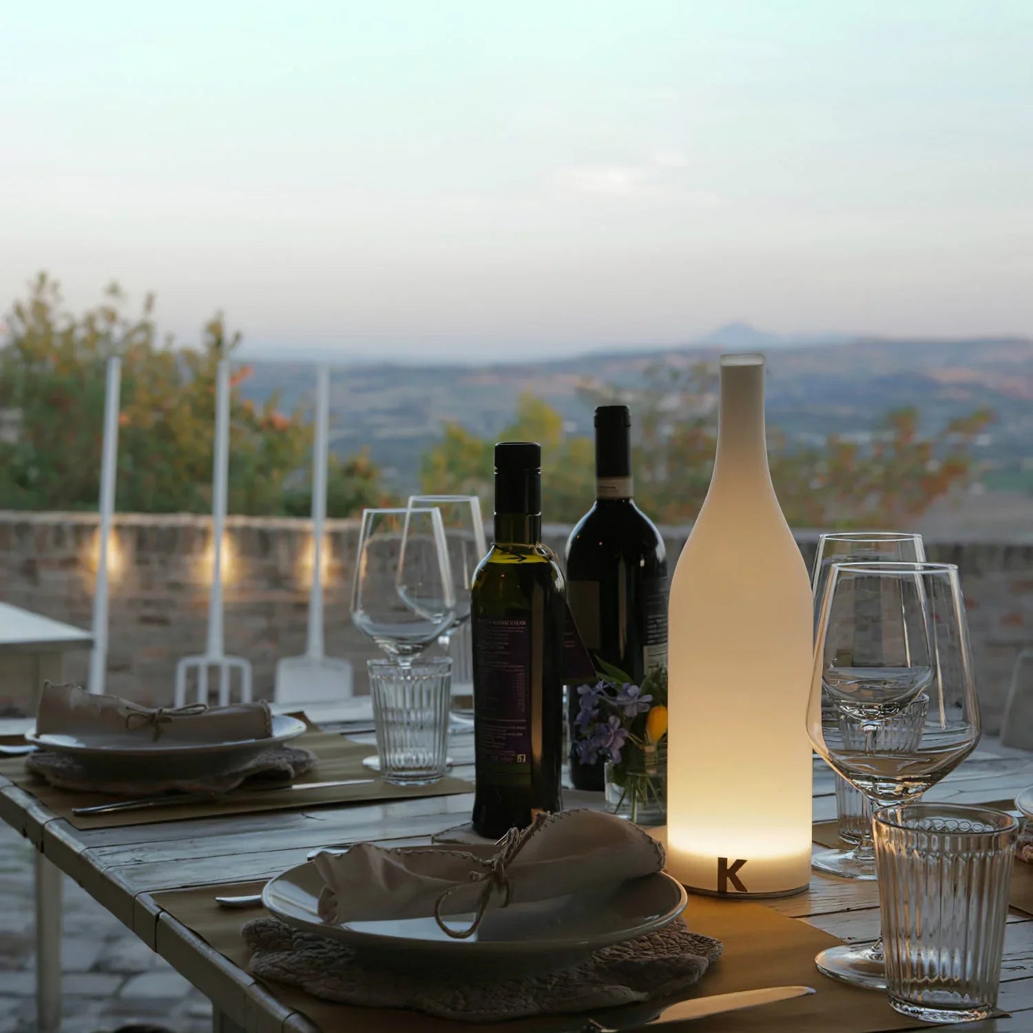 Modern white bottle-shaped table lamp with warm light on outdoor dining table, YH Lamps