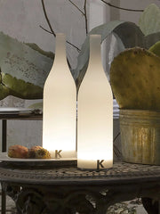 Modern white bottle-shaped table lamps with warm light on an ornate outdoor table near cactus plants