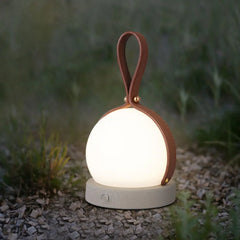 Modern round table lamp with leather handle, glowing outdoors on gravel, YH Lamps
