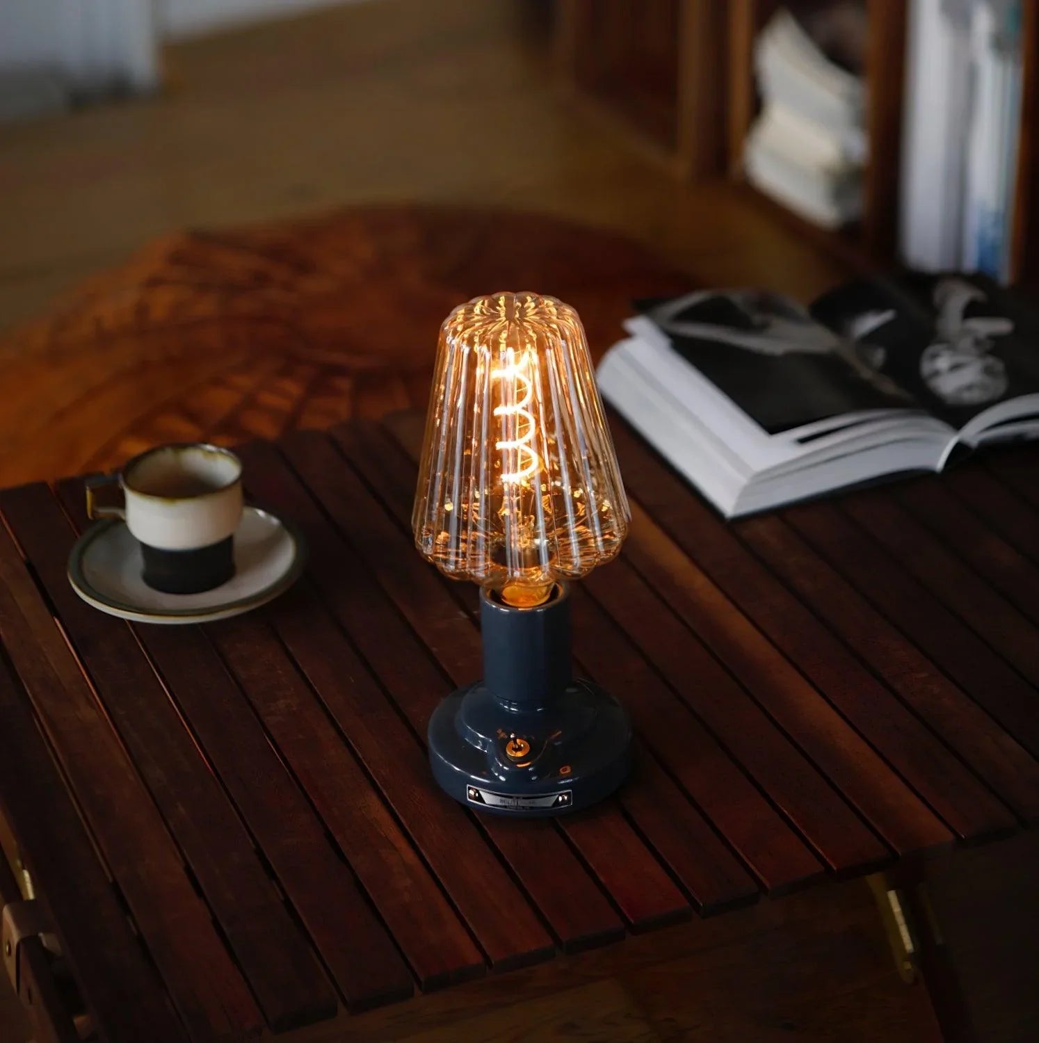 Modern black USB table lamp with glass shade on wooden table, cup and open magazine nearby