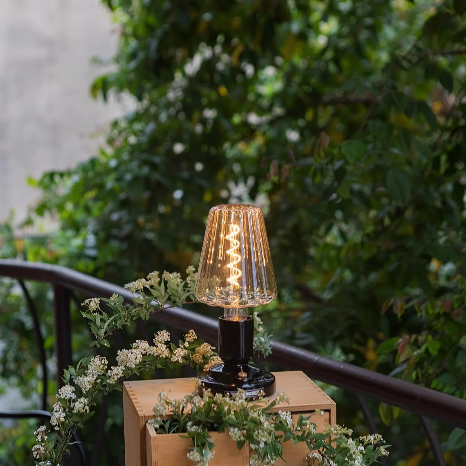 Modern black table lamp with glass shade on outdoor wooden box, surrounded by greenery, YH Lamps