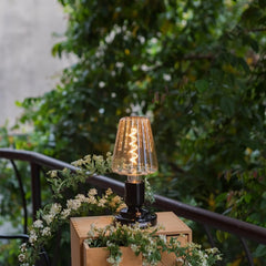 Modern black table lamp with glass shade on outdoor wooden box, surrounded by greenery, YH Lamps