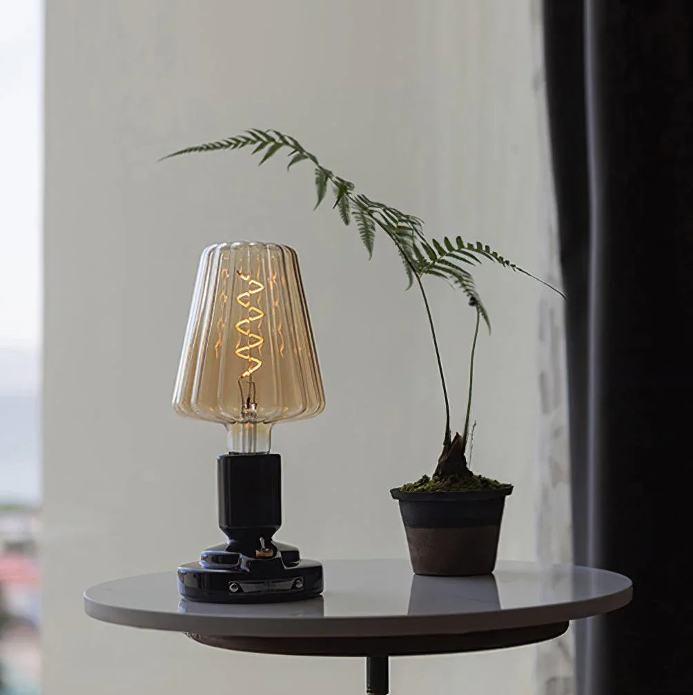 Modern black USB table lamp with ribbed glass shade on a round table next to a small potted plant