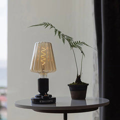 Modern black USB table lamp with ribbed glass shade on a round table next to a small potted plant
