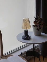 Modern black USB table lamp with glass shade on white round side table near potted plant.