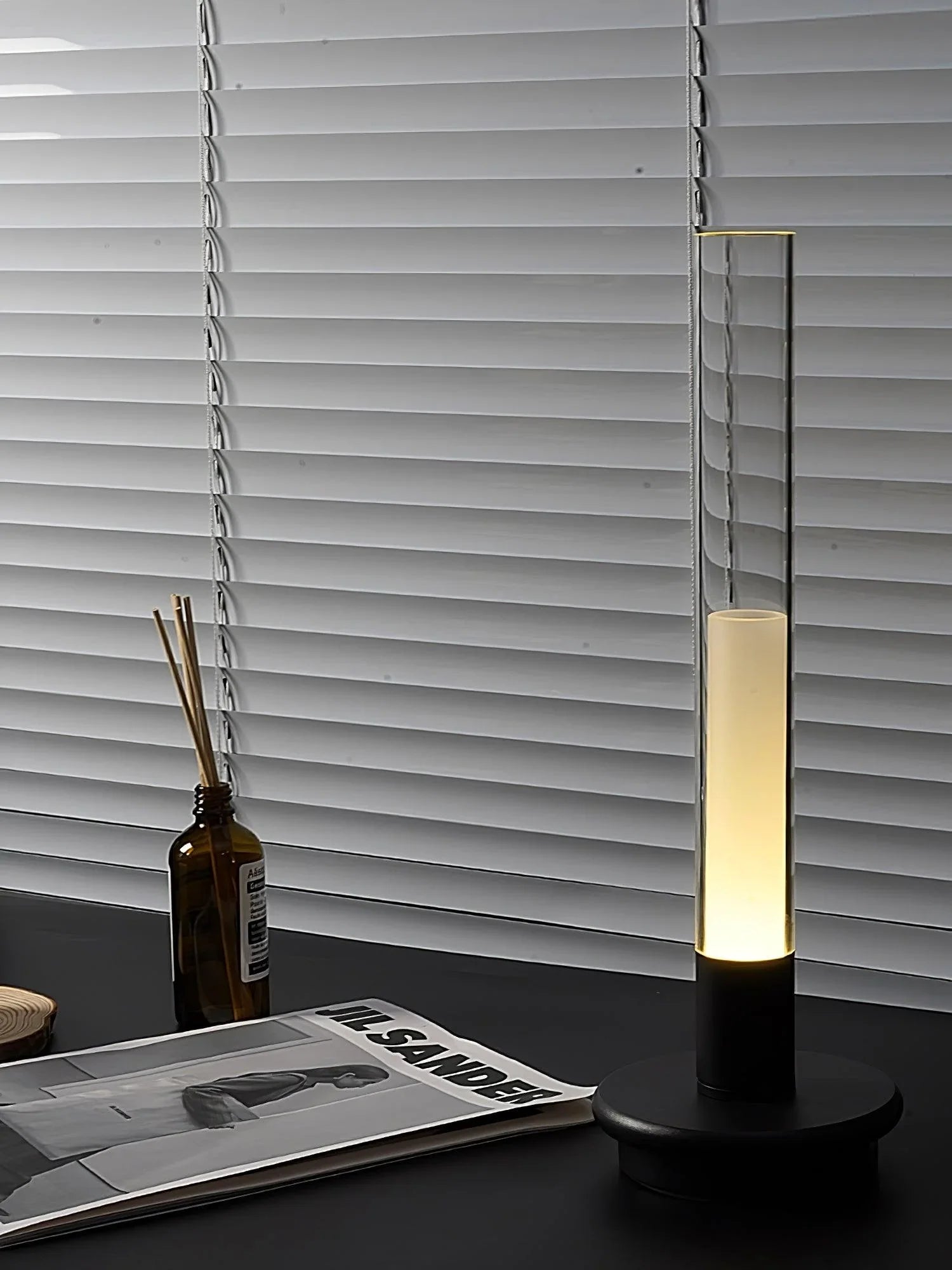 Modern YH Lamps black column table lamp with warm light on desk, blinds in background