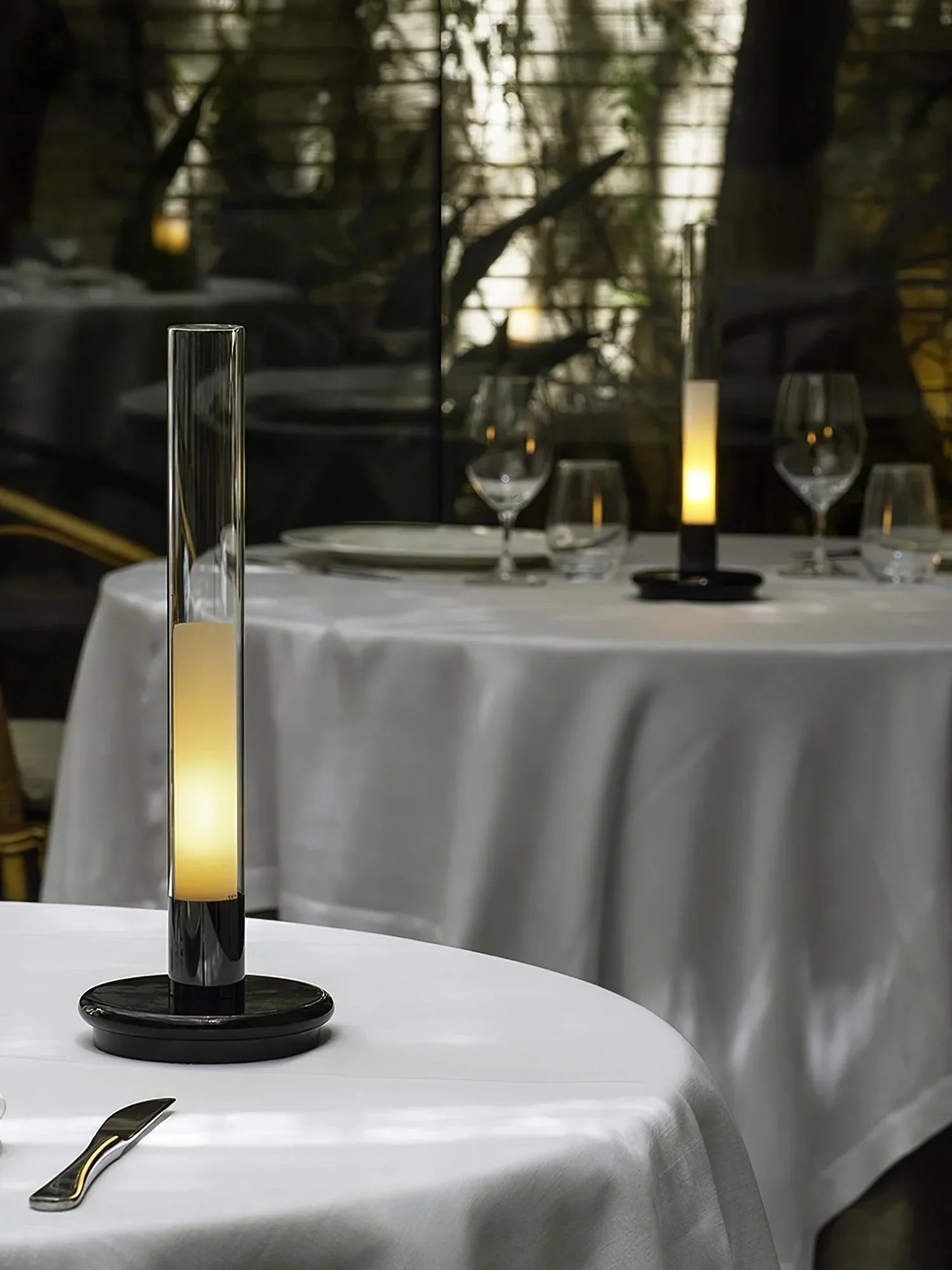 Modern black and clear column table lamp with warm light on a white table at YH Lamps