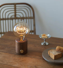 Modern walnut table lamp with round bulb reading 'Oasis' on wooden dining table