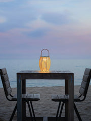 Modern yellow USB lantern table lamp on wooden beach table with two chairs at sunset, YH Lamps