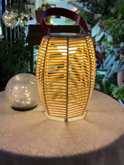Yellow modern USB lantern table lamp with built-in battery on lace table, plants in background