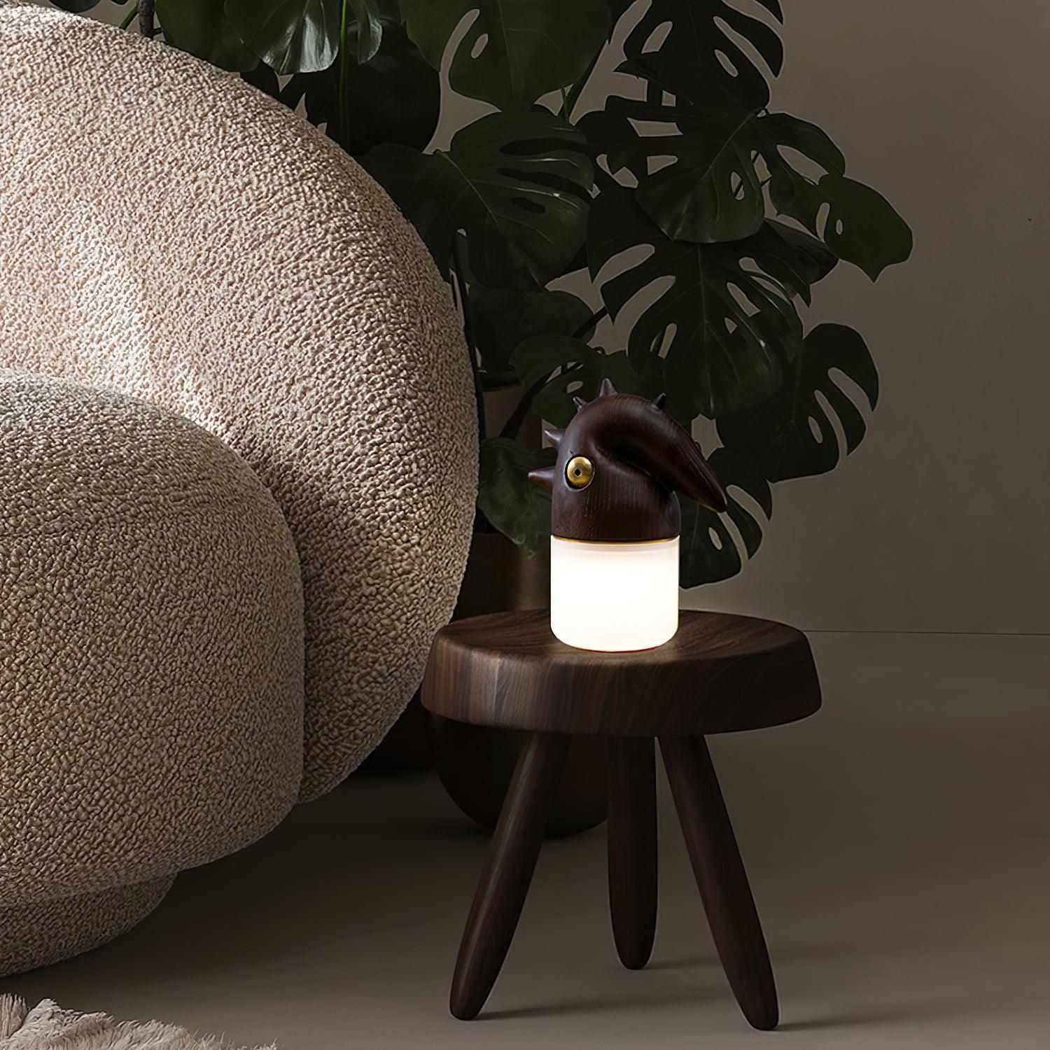 Modern wooden table lamp with warm light on dark side table, next to beige armchair, YH Lamps