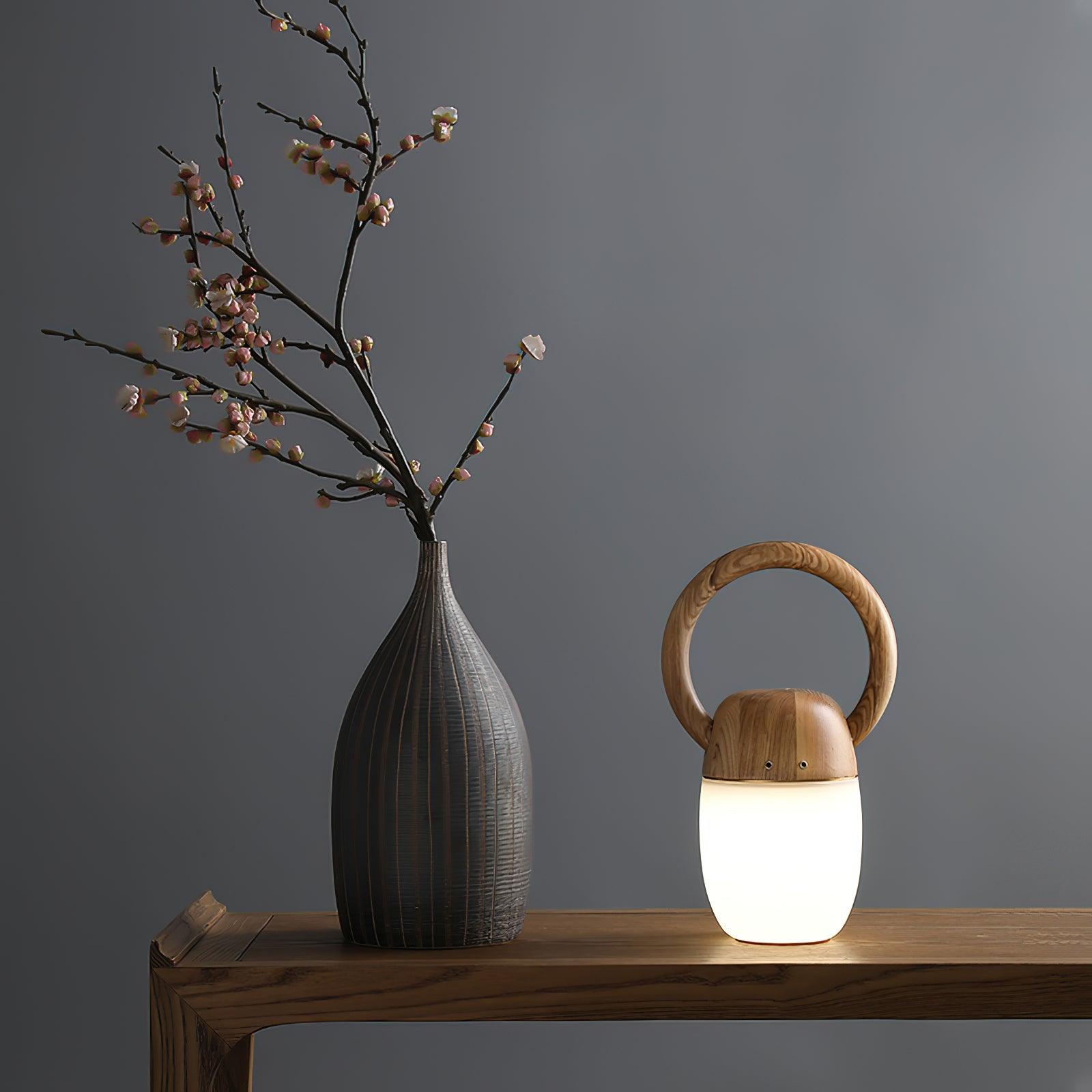 Modern wooden Zen Buddha table lamp with warm light on wooden table beside ceramic vase