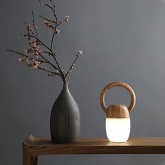 Modern wooden Zen Buddha table lamp with warm light on wooden table beside ceramic vase