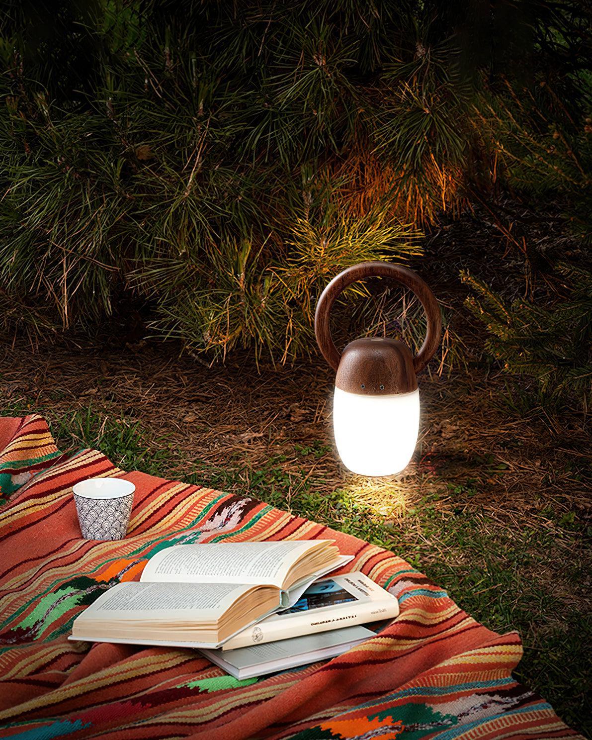 Modern wooden table lamp with warm light on grass next to books and cup, outdoor setting by YH Lamps