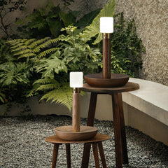Modern wooden table lamps with warm light on round tables in a garden setting, YH Lamps