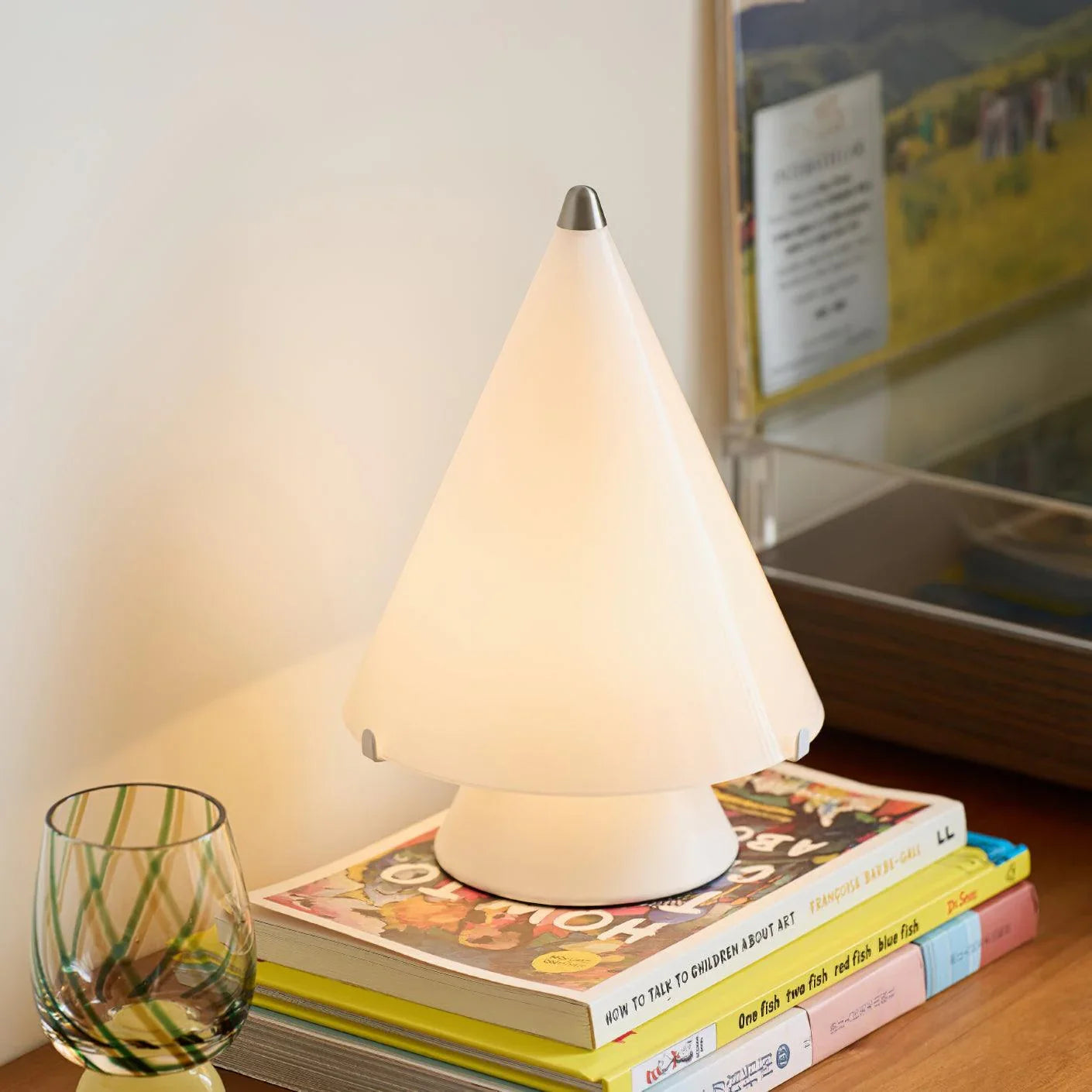 Modern white cone-shaped table lamp with touch switch on wooden surface, styled with books and glass
