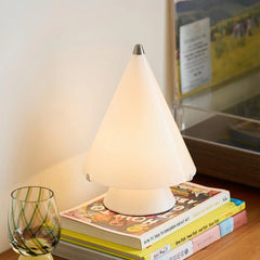 Modern white cone-shaped table lamp with touch switch on wooden surface, styled with books and glass