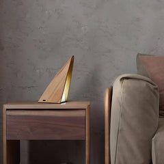 Modern triangular wood table lamp with warm light on wooden side table next to beige sofa