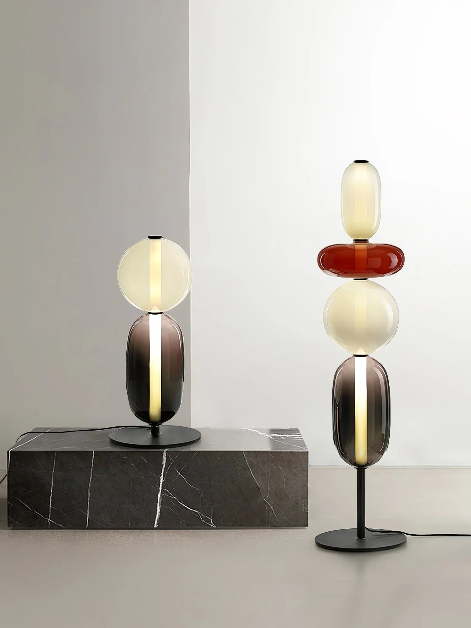 Modern glass table lamps with warm light and black bases on gray marble and floor, minimalist decor
