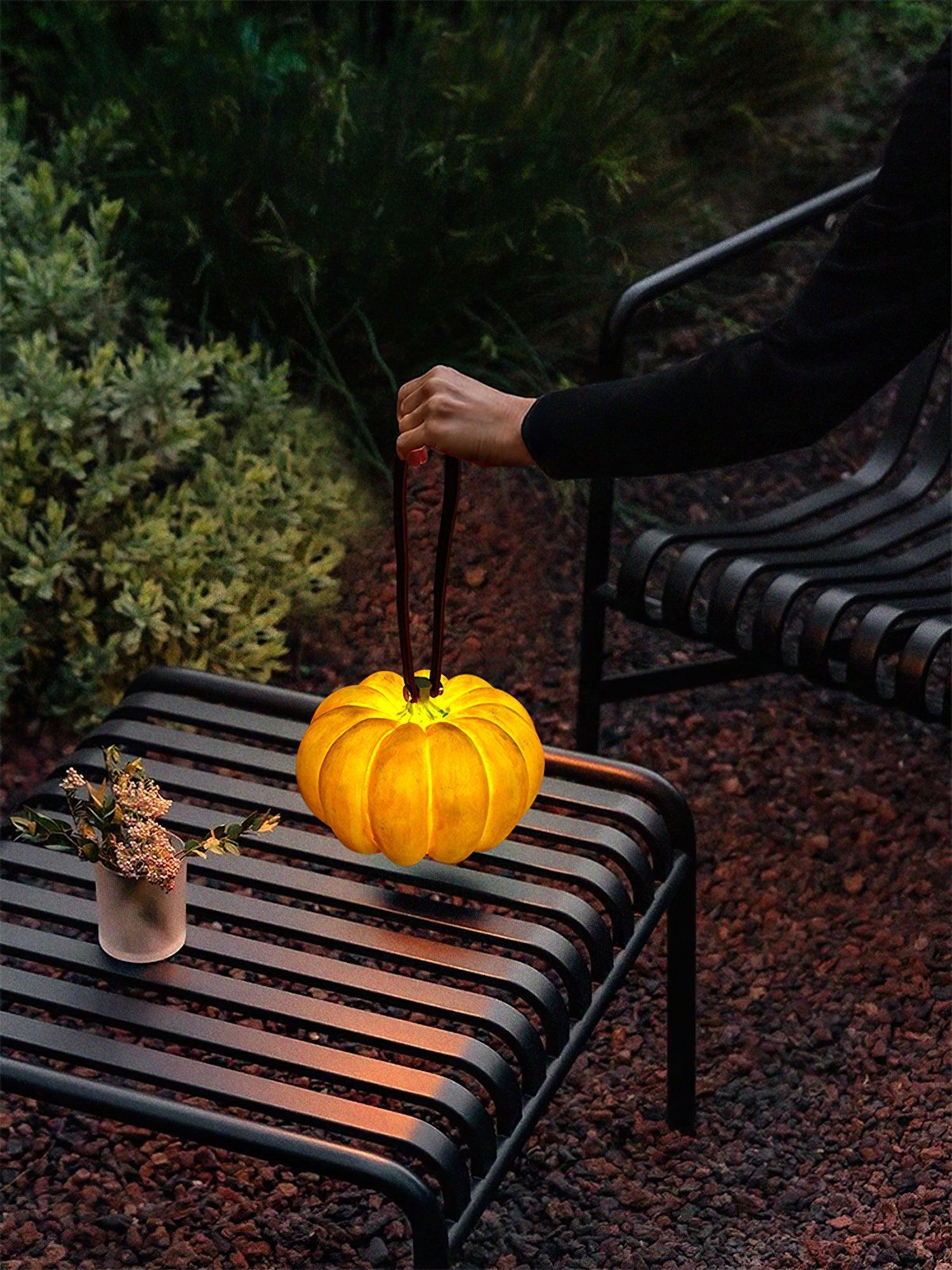 Yellow pumpkin-shaped portable table lamp with handle on outdoor black metal bench at dusk