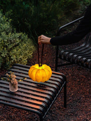Yellow pumpkin-shaped portable table lamp with handle on outdoor black metal bench at dusk