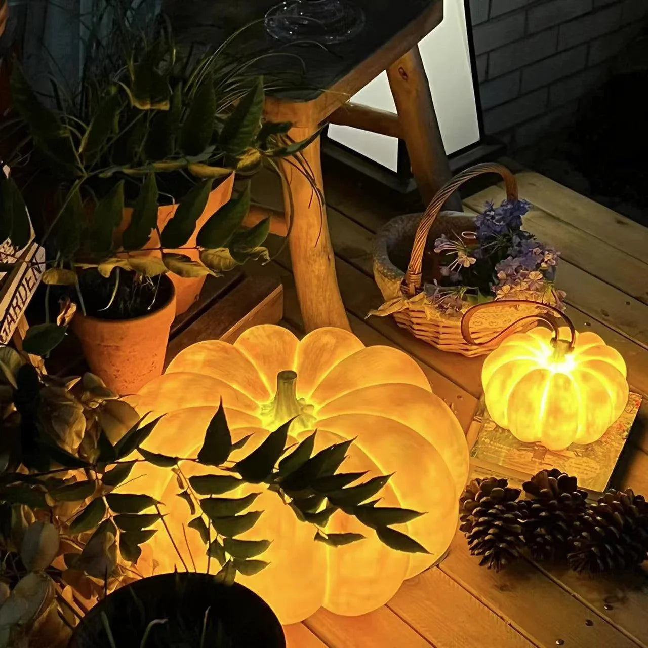Yellow pumpkin-shaped portable table lamps with built-in battery on wooden surface, surrounded by plants and pine cones, from YH Lamps.